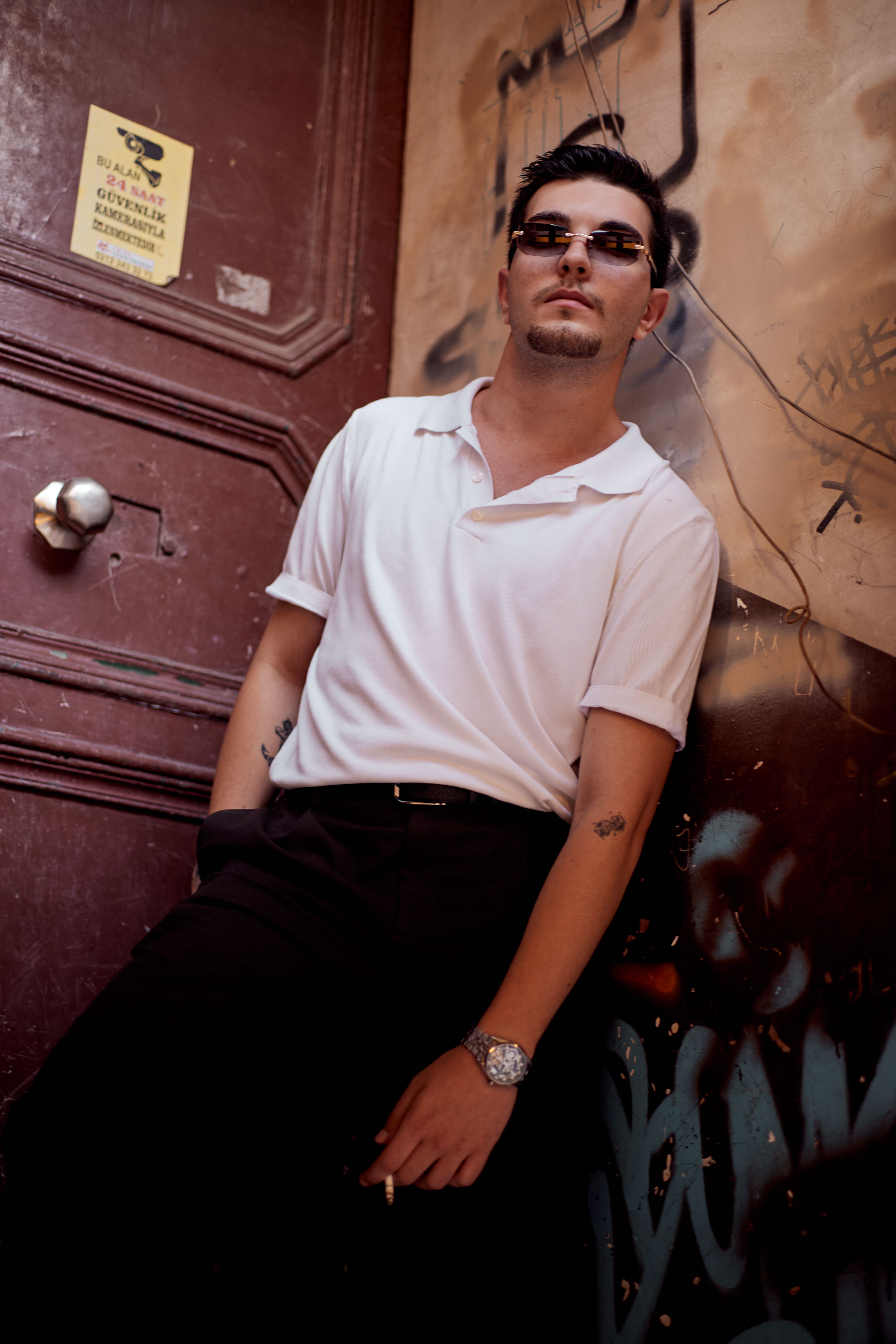 Man in sunglasses poses against a graffiti-covered wall in Istanbul, exuding urban style and confidence.