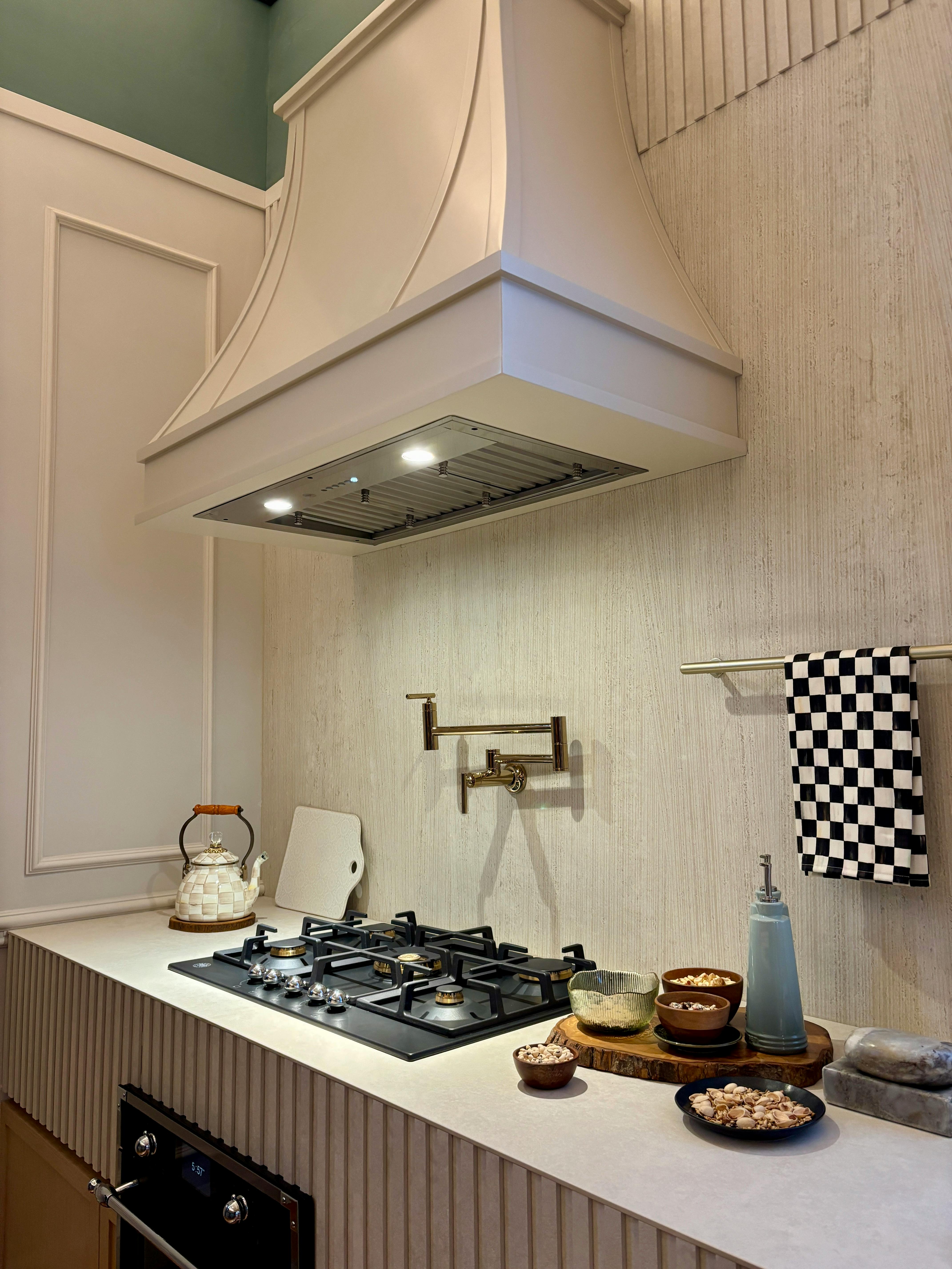 Bright kitchen interior featuring a gas stove and stylish vent hood with utensils and bowls under warm lighting.