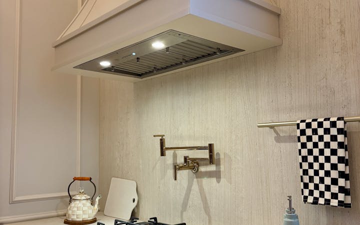 Bright kitchen interior featuring a gas stove and stylish vent hood with utensils and bowls under warm lighting.