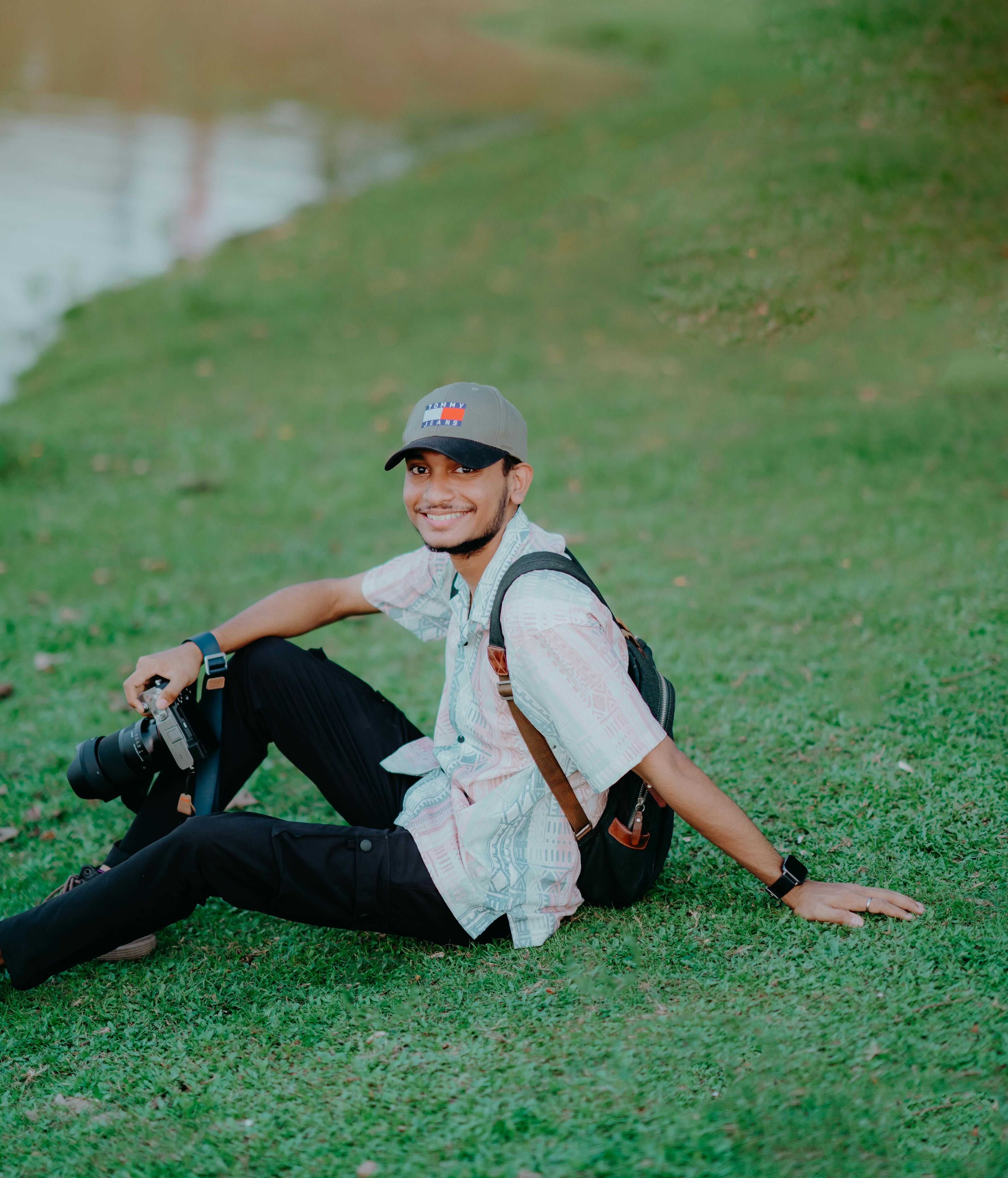 Smiling young adult photographer sitting on grass holding camera.