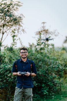 Young man controls a drone in a vibrant outdoor setting with lush greenery.