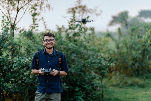 Young man joyfully flying a drone in a lush outdoor setting. Nature meets technology.