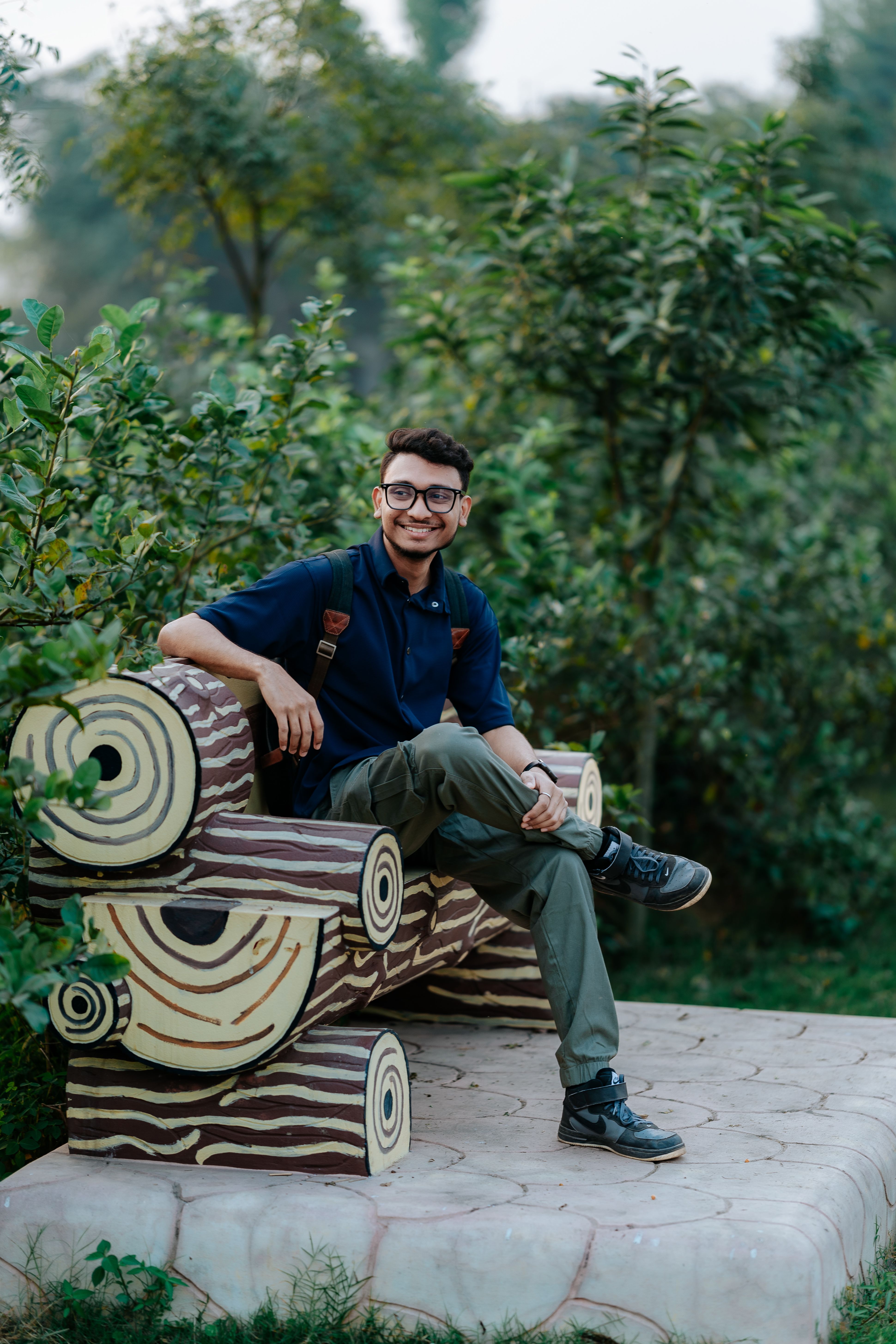 Young man smiles while sitting on a creatively designed bench outdoors.