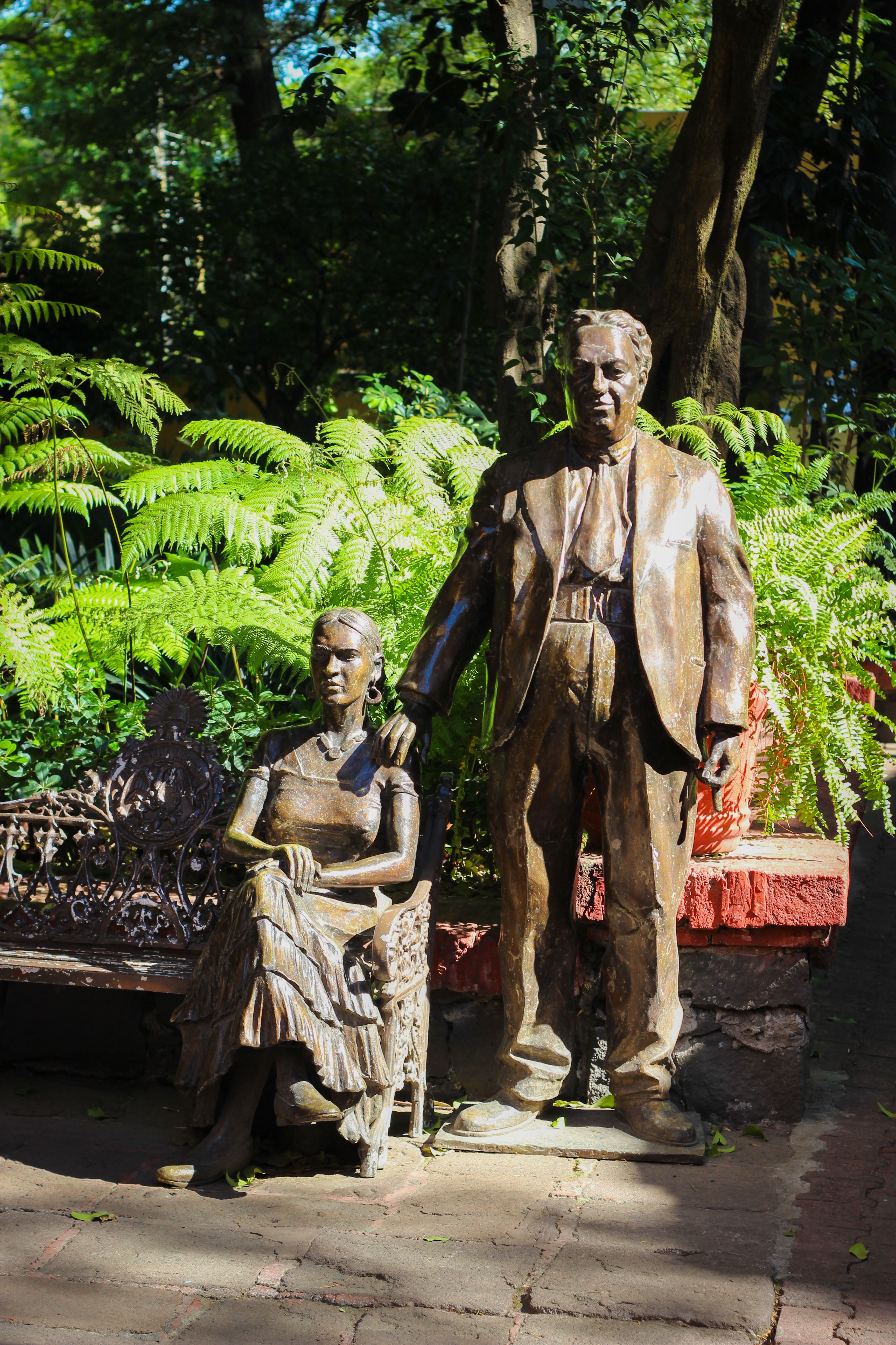 Bronze statues of two iconic Mexican artists sitting and standing in a lush garden.