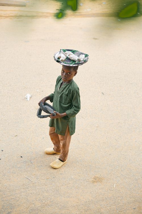 Free A young boy balances a basket on his head on a sandy path, showcasing skill and balance. Stock Photo