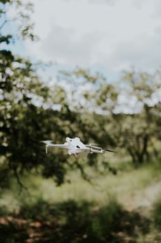 Aerial shot of a white drone navigating through a dense green forest on a sunny day.