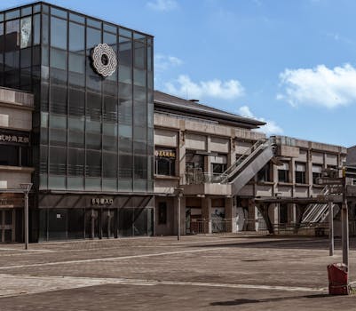 Empty outdoor plaza in front of a modern shopping center with a glass facade and clear blue sky.