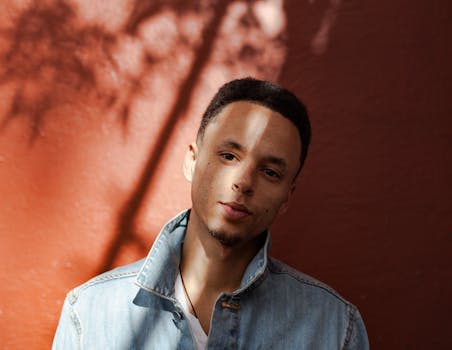 一位穿着牛仔夹克的年轻人，在温暖阳光与阴影交织的背景中，展现出时尚的肖像