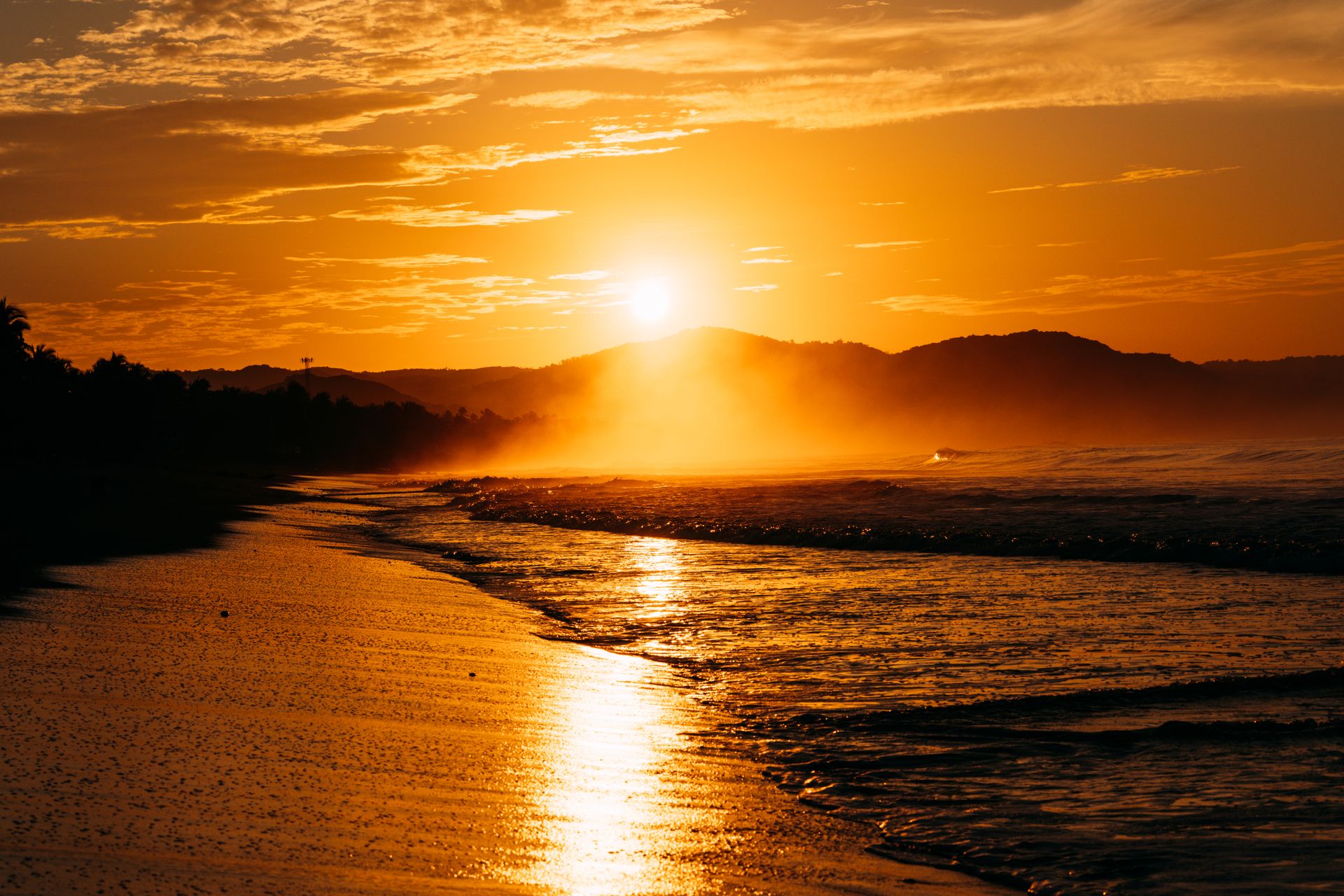 Breathtaking sunset reflecting over the ocean waves and sandy shoreline, creating a golden glow.