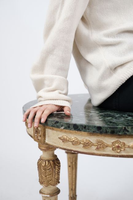 A close-up of a person's hand resting on a luxurious green marble and gold table.