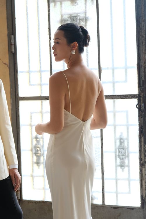 Free An elegant woman in a white dress stands by a vintage window, exuding grace and style. Stock Photo