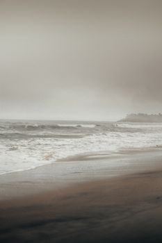 A tranquil misty beach scene at dusk with gentle waves and a cloudy sky, conveying a soothing autumn ambiance.