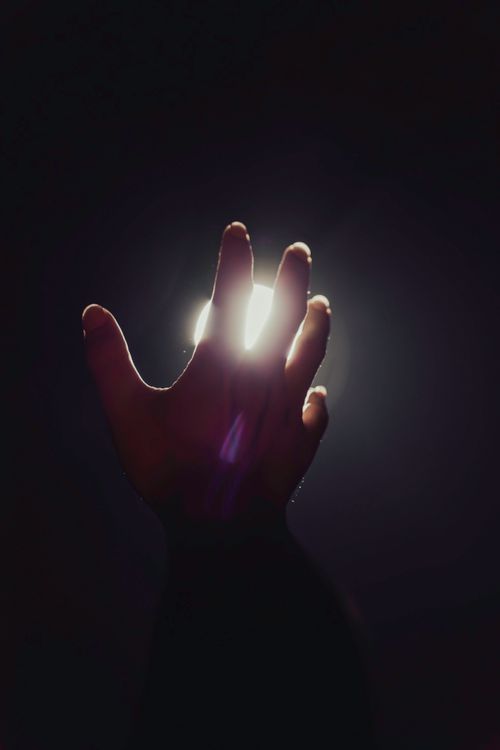 Free A silhouette of a hand reaching towards a bright light, symbolizing hope and aspiration. Stock Photo