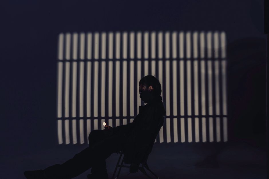 Silhouette cast in shadow bars — isolation and confinement