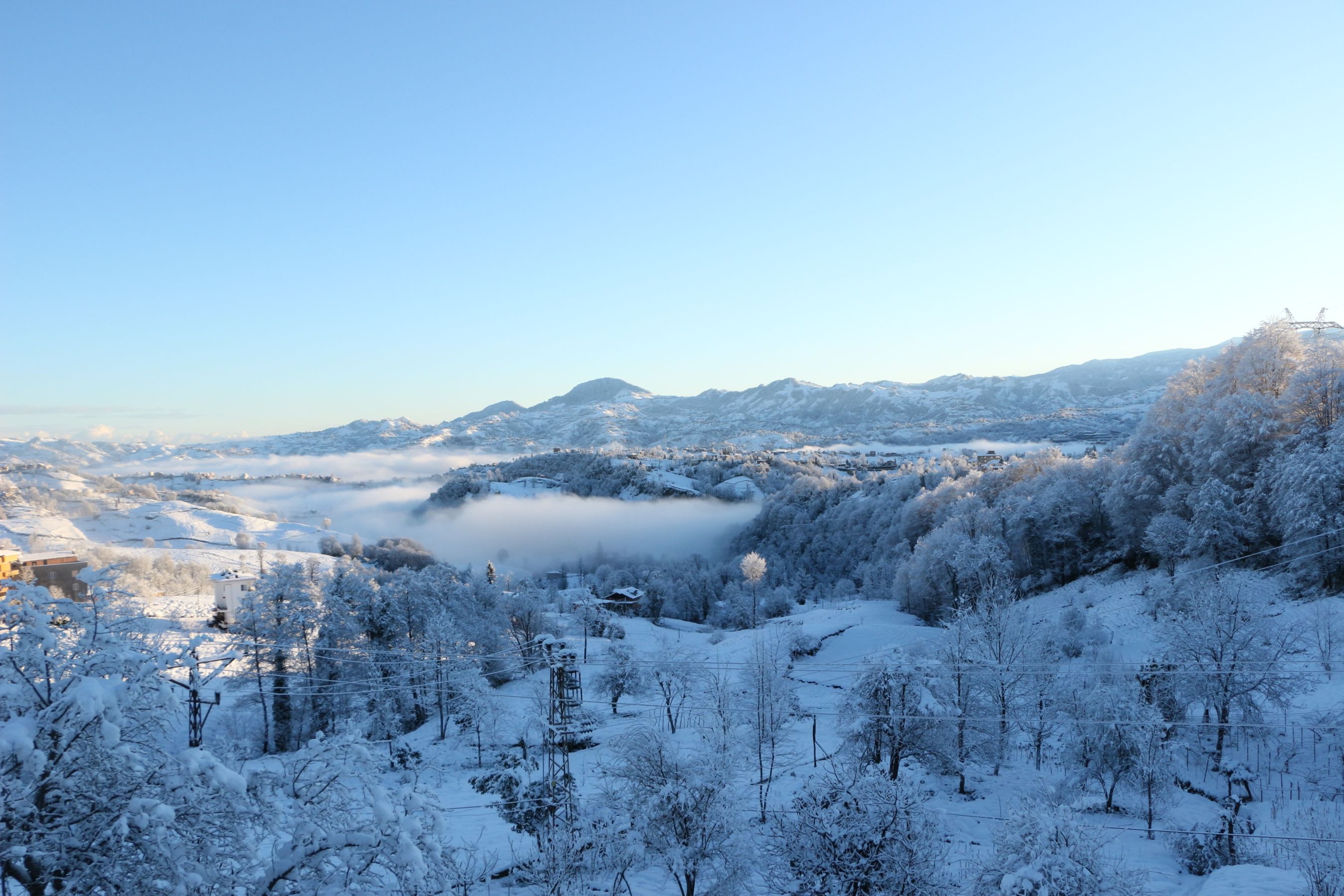 A breathtaking view of a snow-covered mountain landscape under a clear blue sky at sunrise.