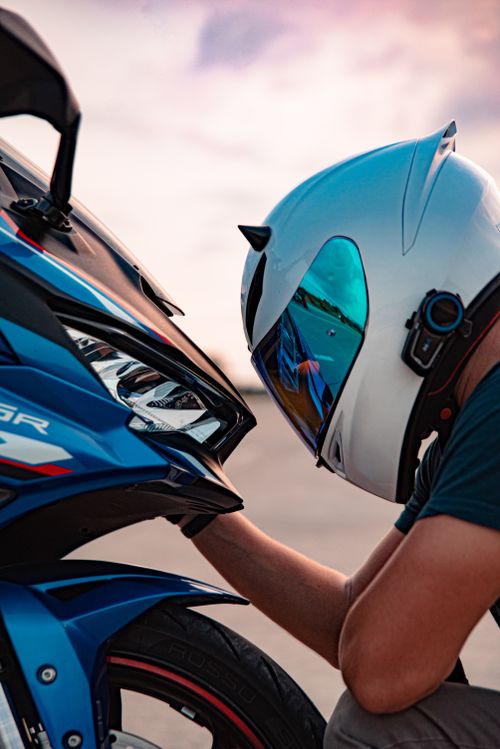 Free A motorcycle rider, wearing a helmet, examines a blue sport bike at sunset in Bali. Stock Photo
