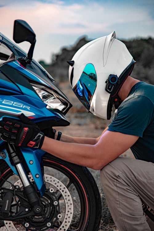 Free A motorcyclist wearing a helmet checks a blue sports motorcycle outdoors in Bali, Indonesia. Stock Photo
