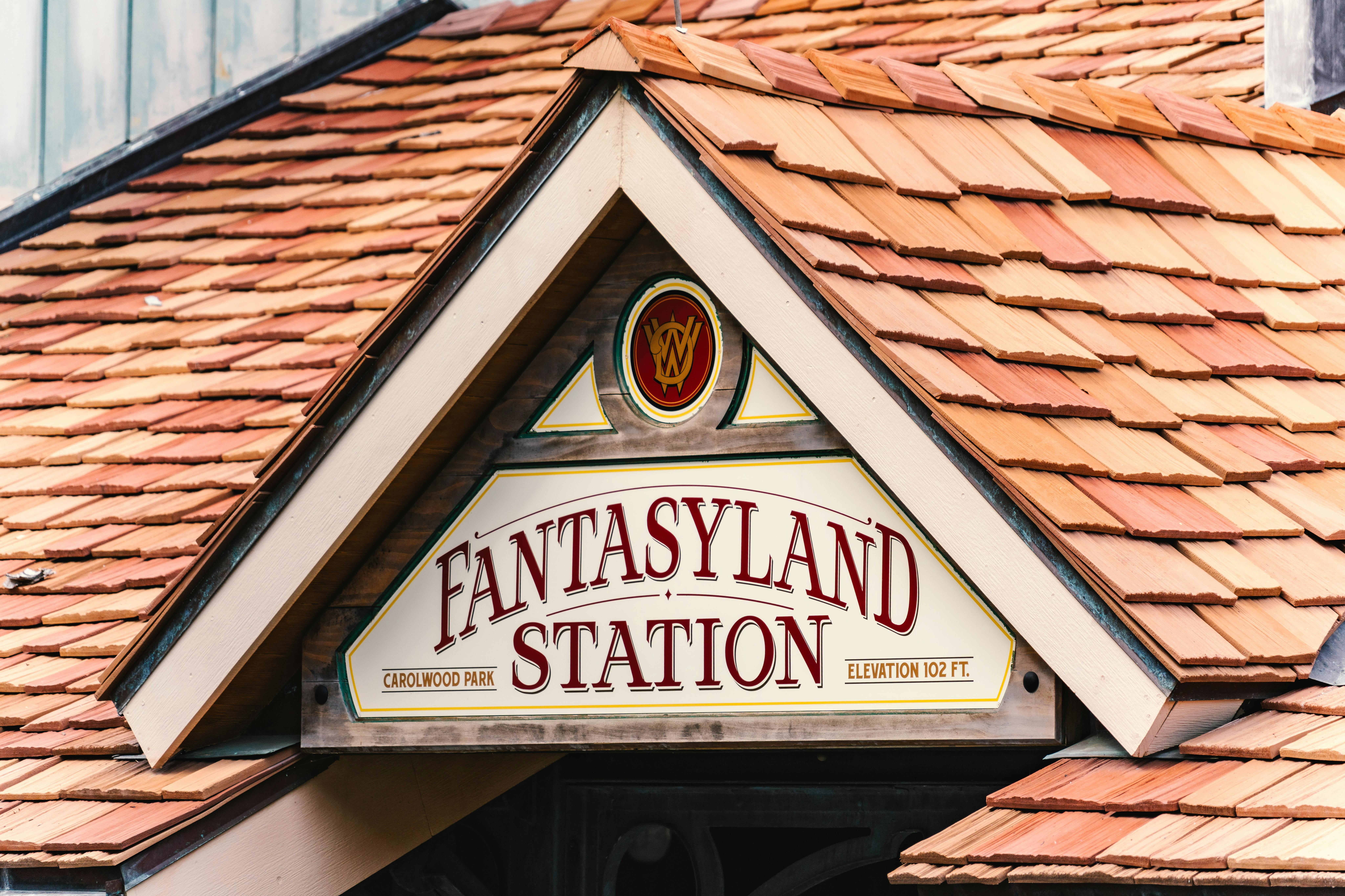 Close-up of a Fantasyland Station sign with classic wooden shingle roofing in Florida.