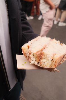 Person holding a fresh sandwich on the street, showcasing outdoor urban lifestyle.