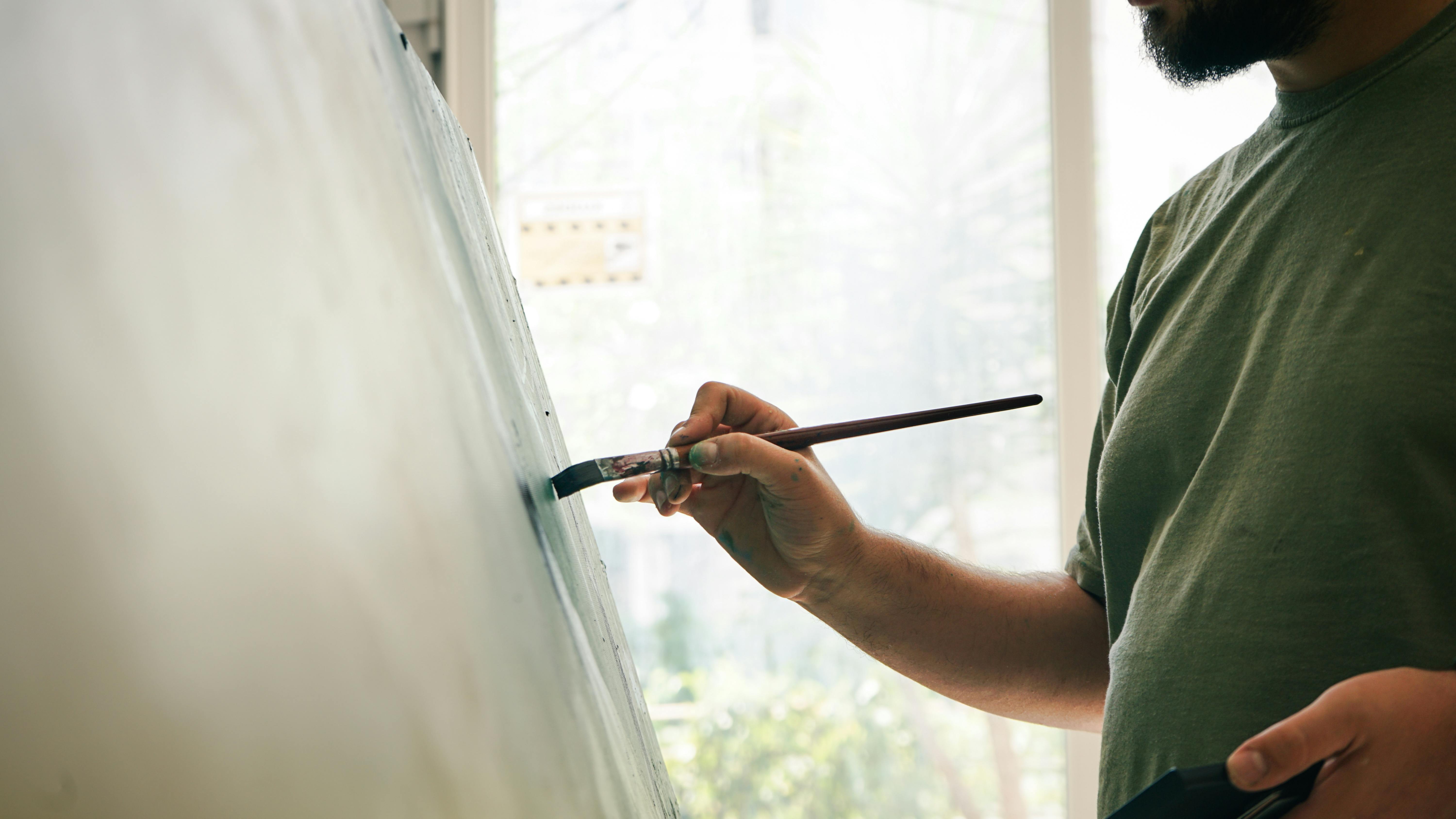 Male artist painting on a canvas in a bright studio, focusing on his creative work.