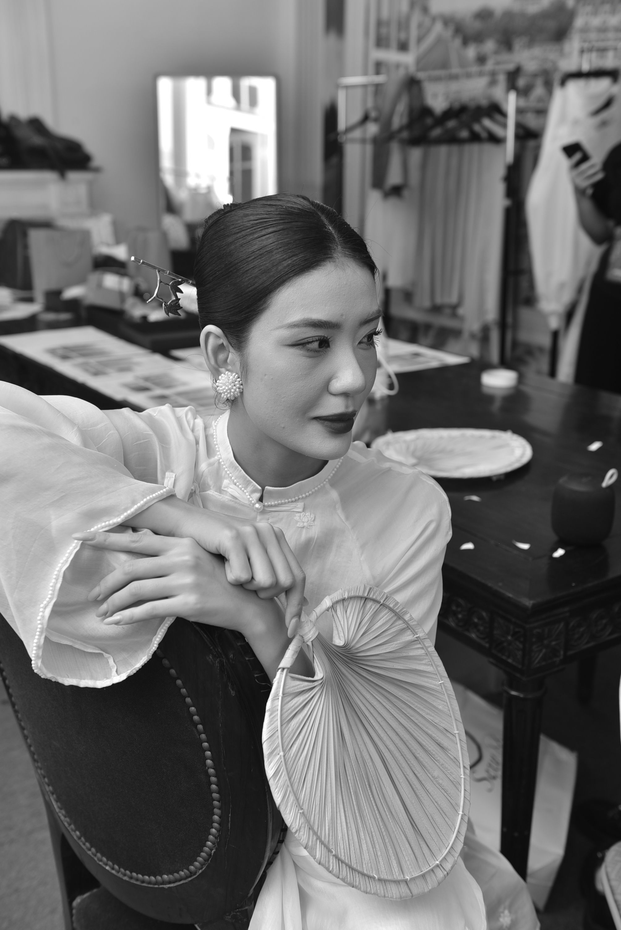 Black and white portrait of a woman in traditional clothing holding a decorative fan indoors.