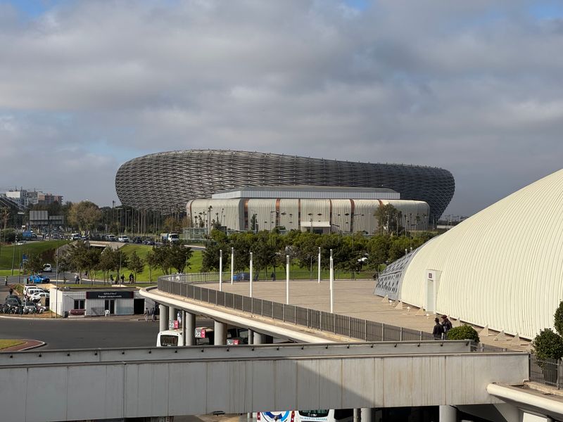 The Prince Moulay Abdellah stadium in Rabat, its curved metal lattice facade seen across the sports complex under a cloudy sky.