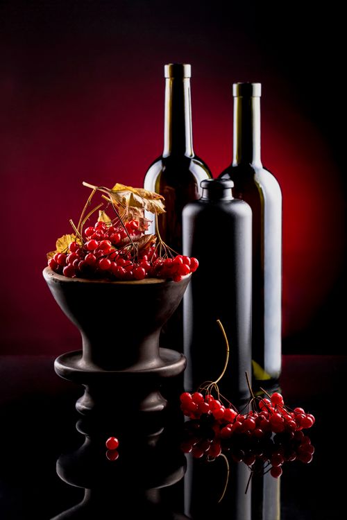 Free Artistic still life of red berries and wine bottles on a reflective surface. Stock Photo