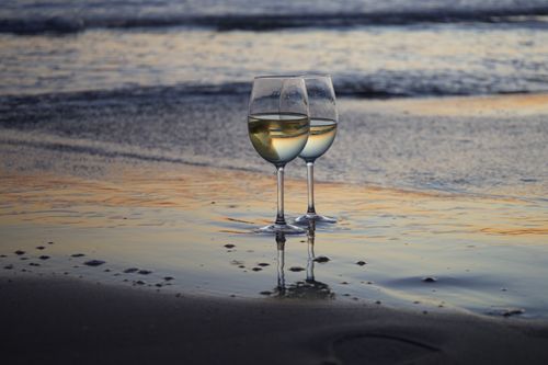 Free Two glasses of white wine on a beach during a serene sunset, reflecting warm colors. Stock Photo