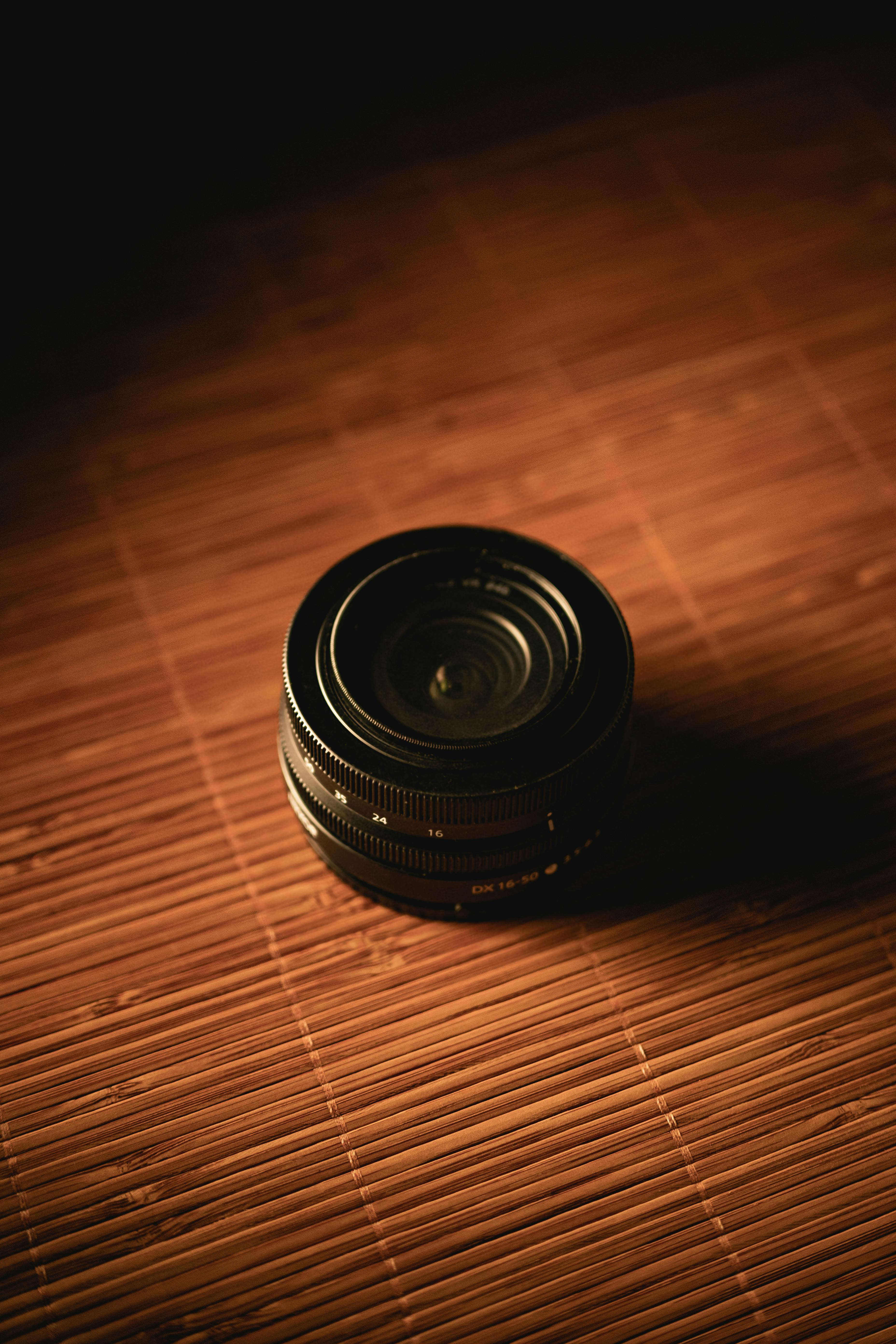 Gratis Pengambilan gambar artistik lensa kamera yang diletakkan di atas tikar bambu dengan pencahayaan dramatis. Foto Stok