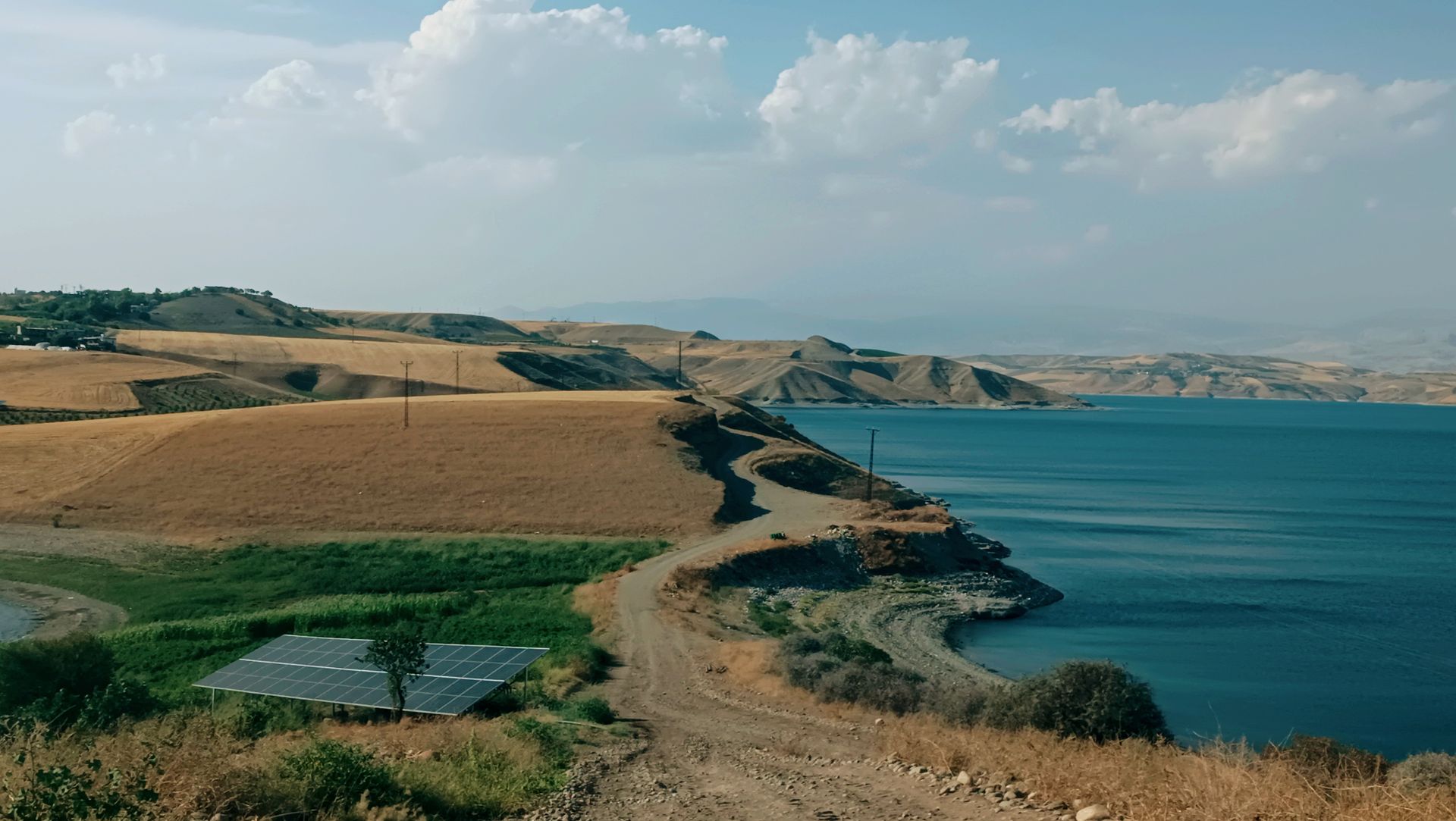 A serene rural landscape with solar panels near a lake under a bright sky.