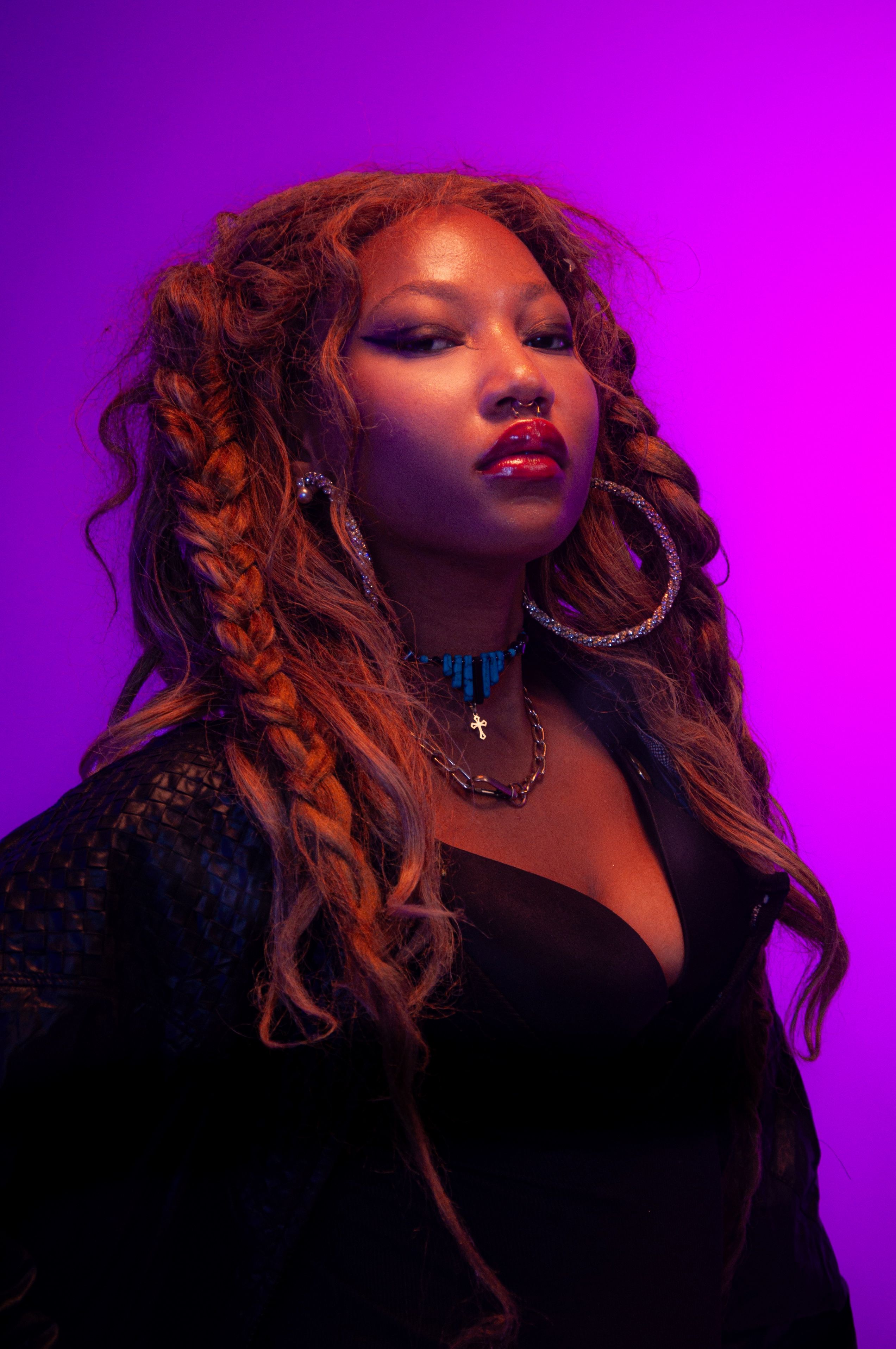 Stylish woman with braided hair and statement jewelry in a vibrant purple setting.
