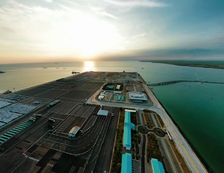 A stunning aerial view of an industrial port during sunrise, showcasing expansive docks and ocean horizon.