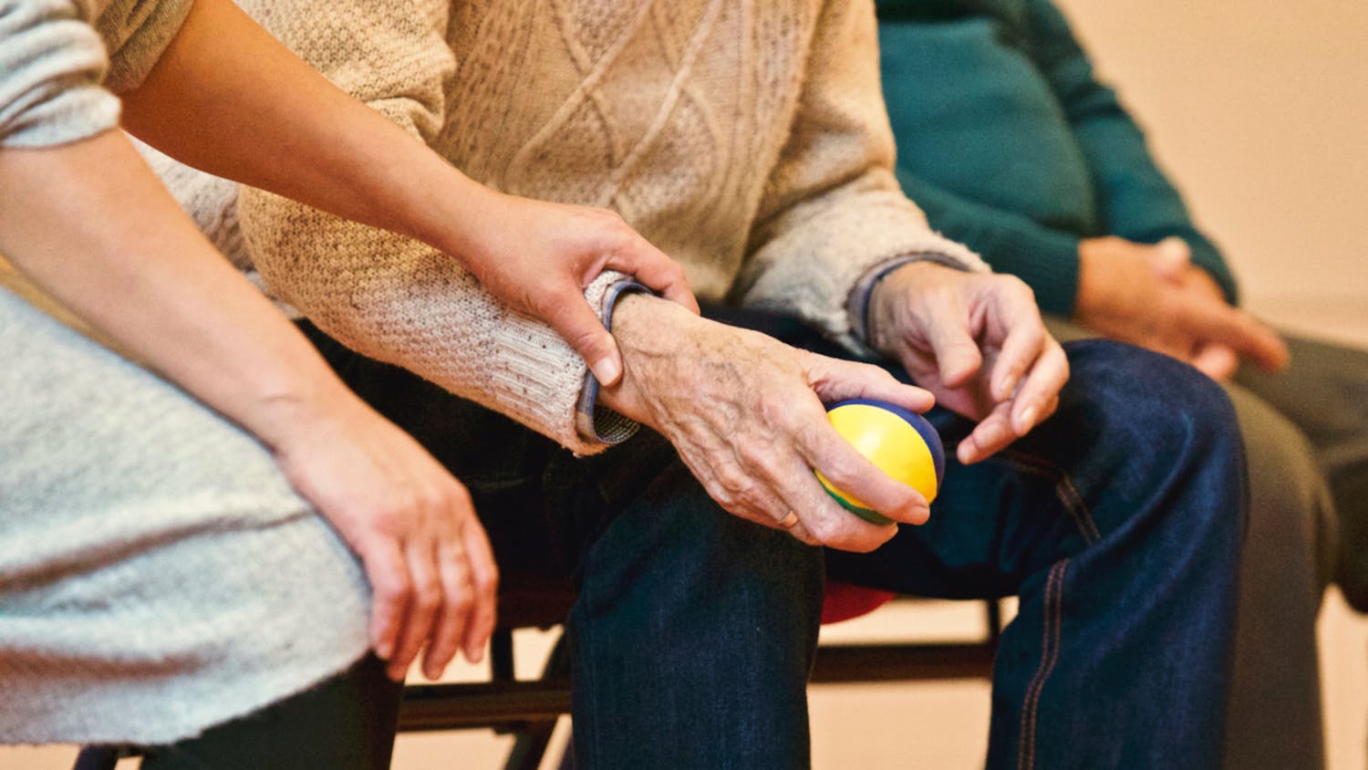 An elderly person receives support from a caregiver, holding hands indoors, showcasing compassion