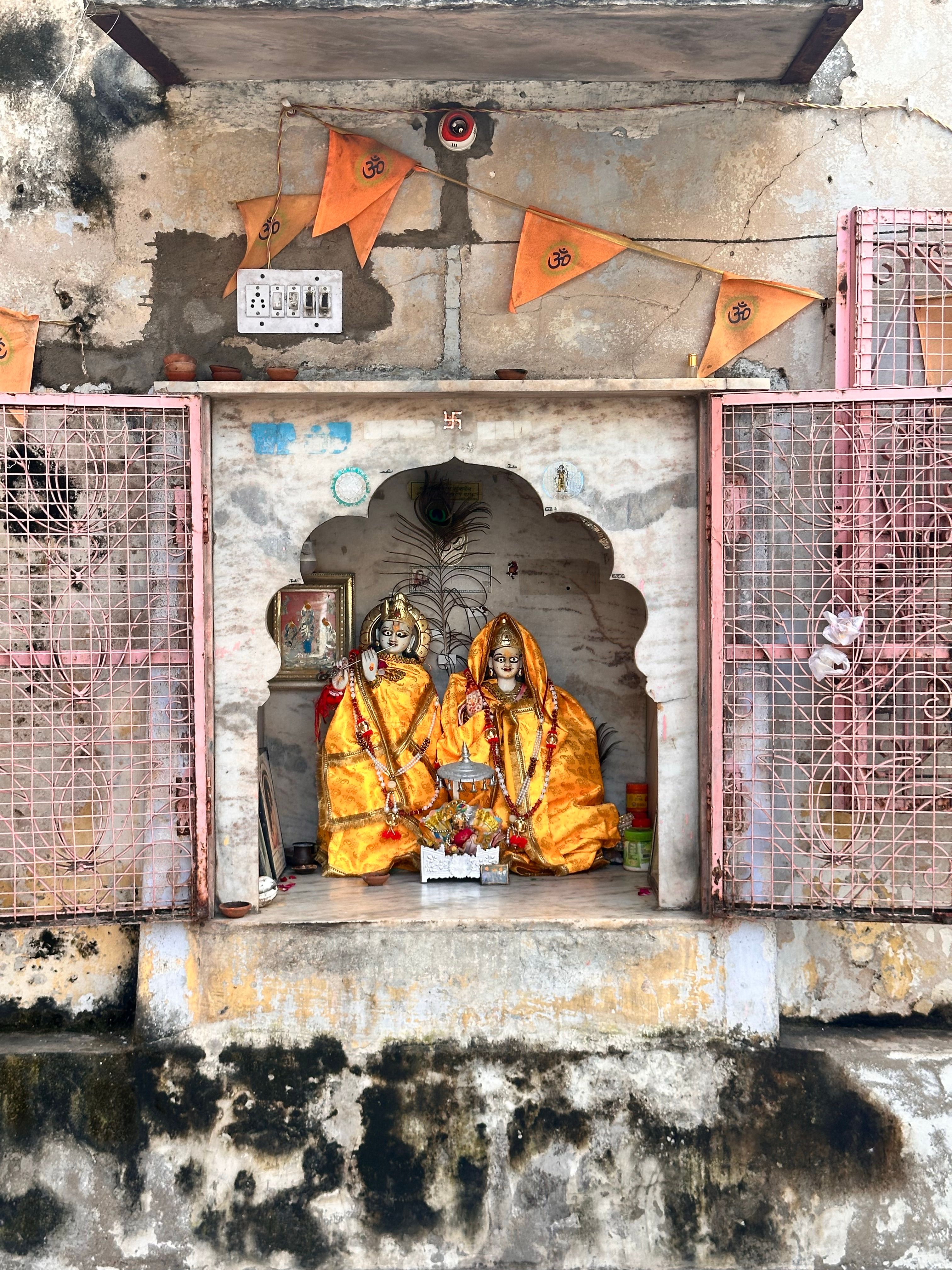 Ornate Hindu shrine with vibrant idols and flags on rustic wall.