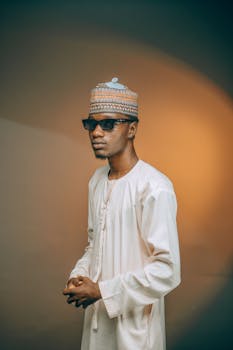 Portrait of a stylish Nigerian man in traditional attire wearing sunglasses against a warm backdrop.
