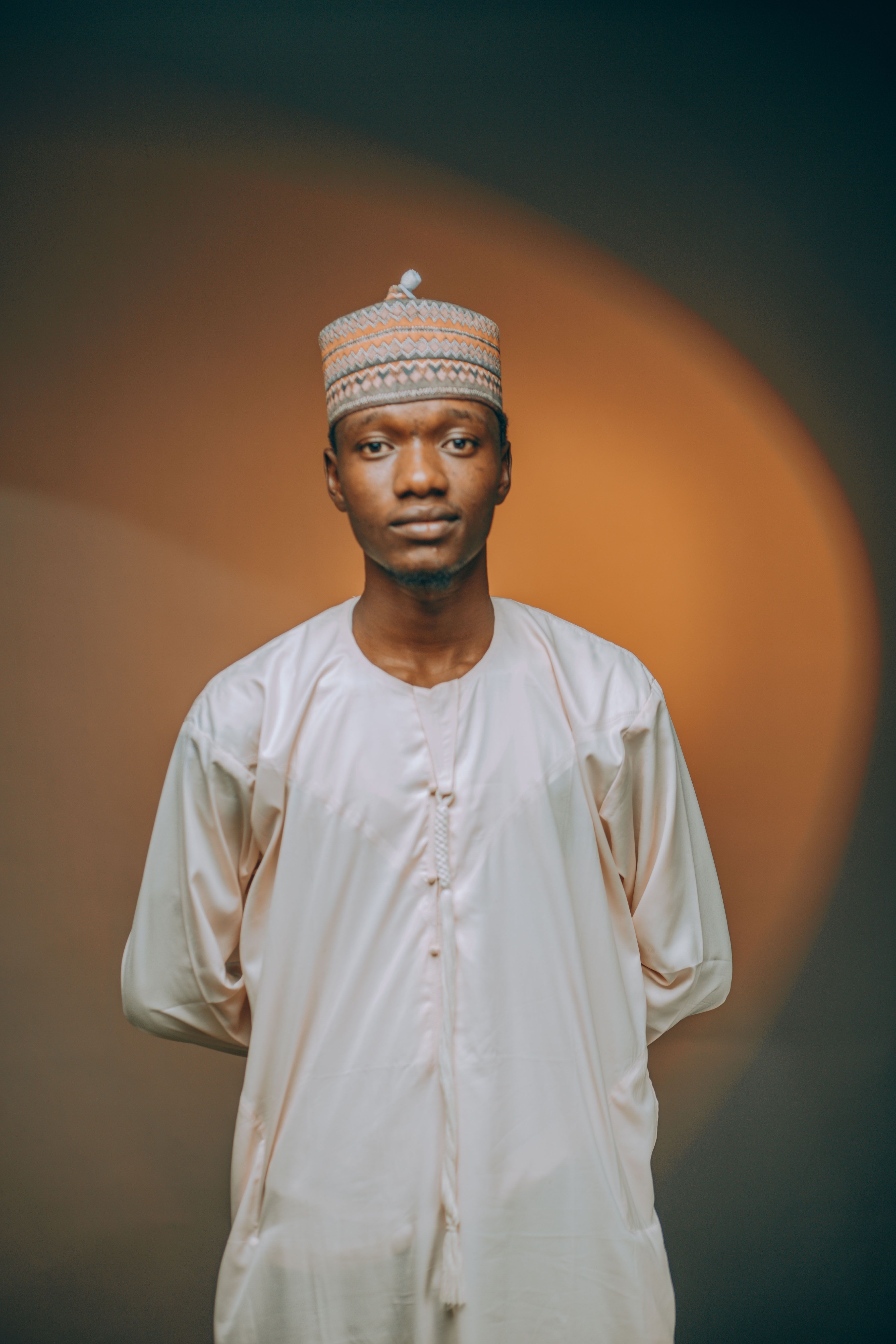 A Nigerian man dressed in traditional attire poses indoors for a portrait.