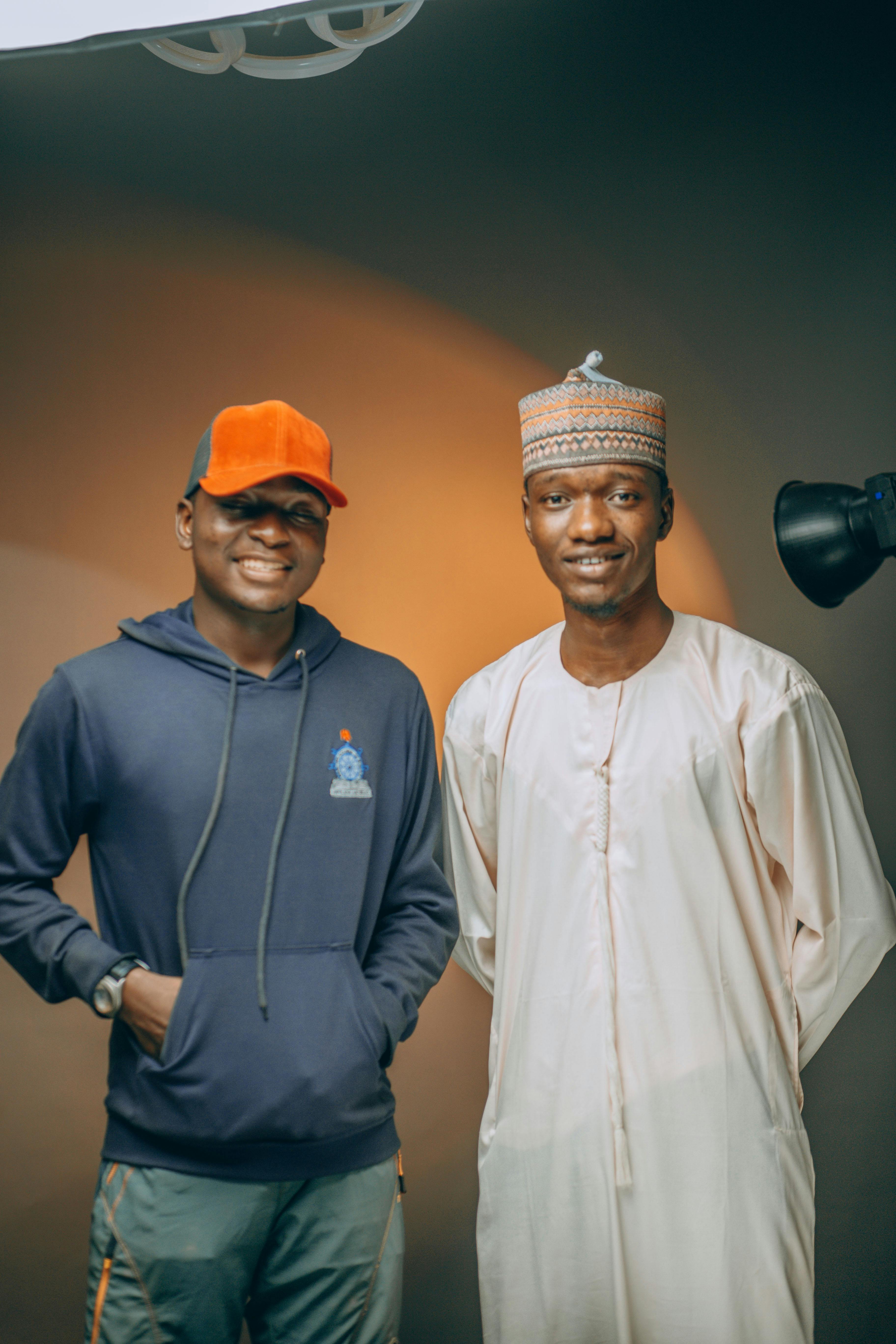 Two smiling men posing indoors in Nigeria, showcasing traditional and modern fashion styles.