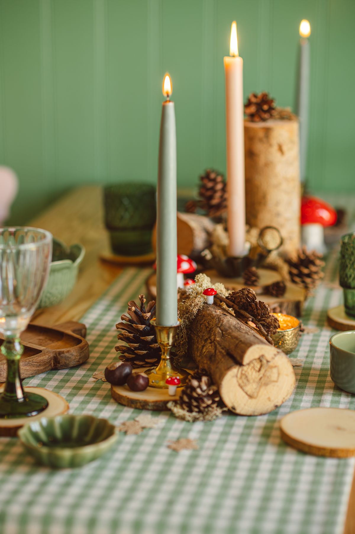 Low autumn table centerpiece with pinecones and taper candles on a plaid cloth that keeps sightlines clear