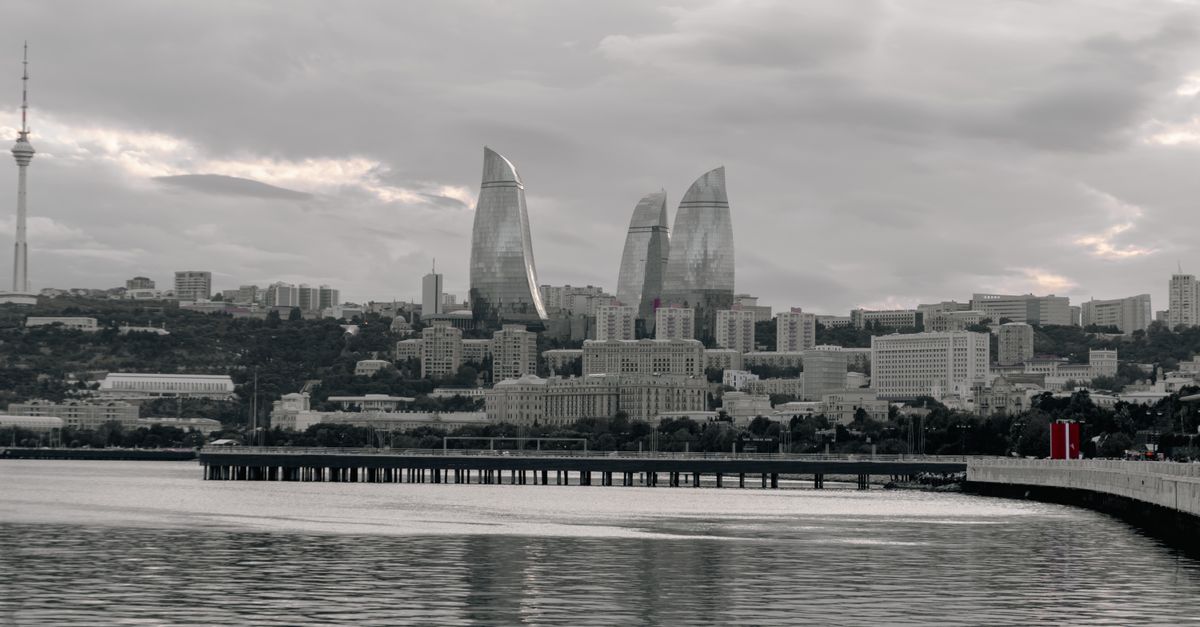 The striking silhouette of Baku's Flame Towers against a dramatic sky, viewed from the Caspian Sea.