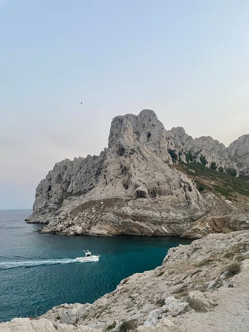 Dramatic coastal cliffs with a boat cruising on clear blue waters under a calm sky.