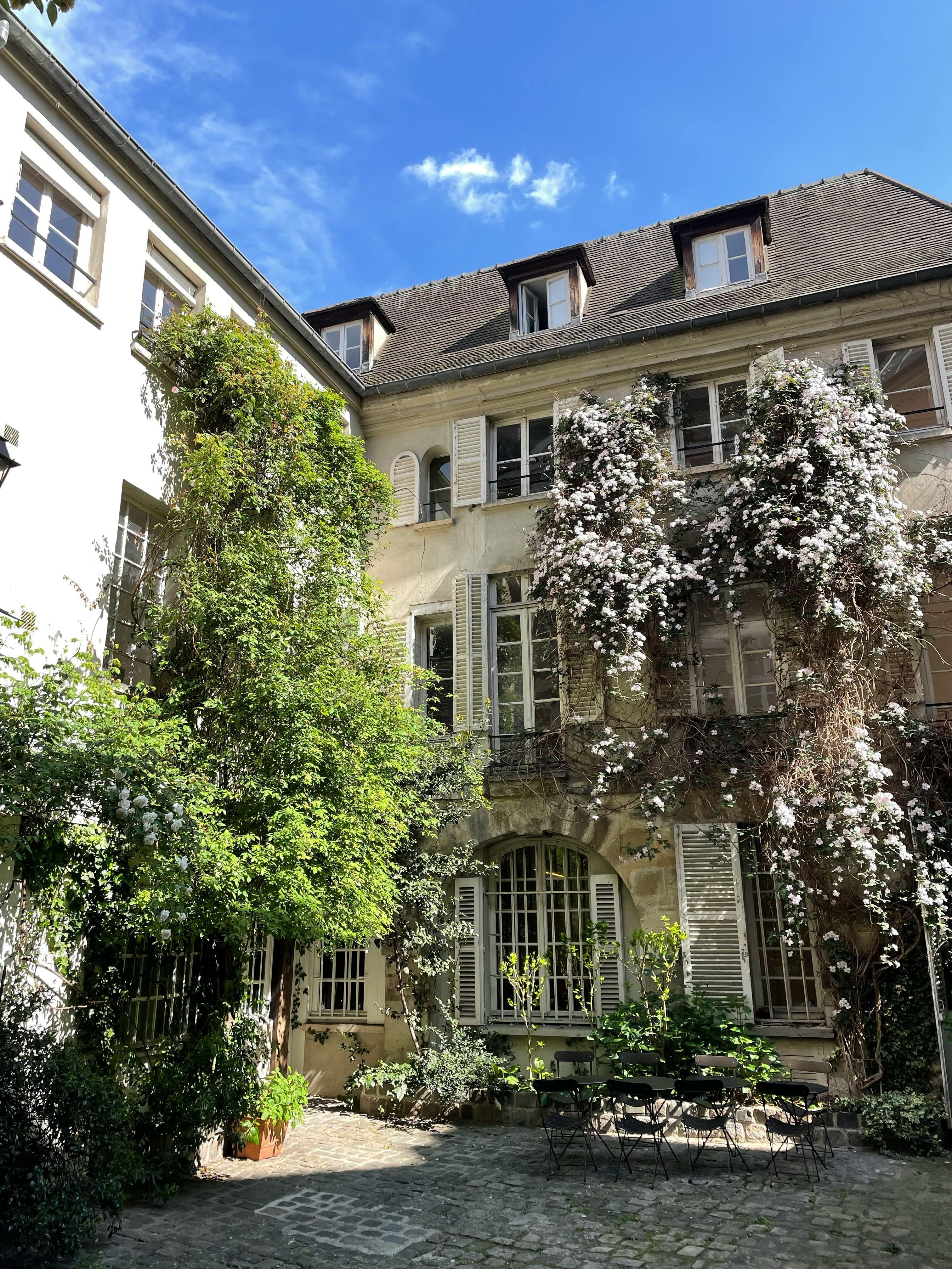 Lush greenery and flowers adorn a charming historic courtyard under a bright blue sky.
