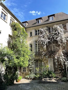 Lush greenery and flowers adorn a charming historic courtyard under a bright blue sky.