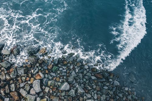 Free Serene aerial view of ocean waves crashing onto a rocky seashore, depicting the natural beauty of coastlines. Stock Photo