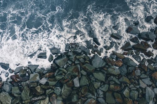 Free Aerial shot capturing waves crashing over rugged rocks on a seashore, showcasing the ocean's natural beauty. Stock Photo