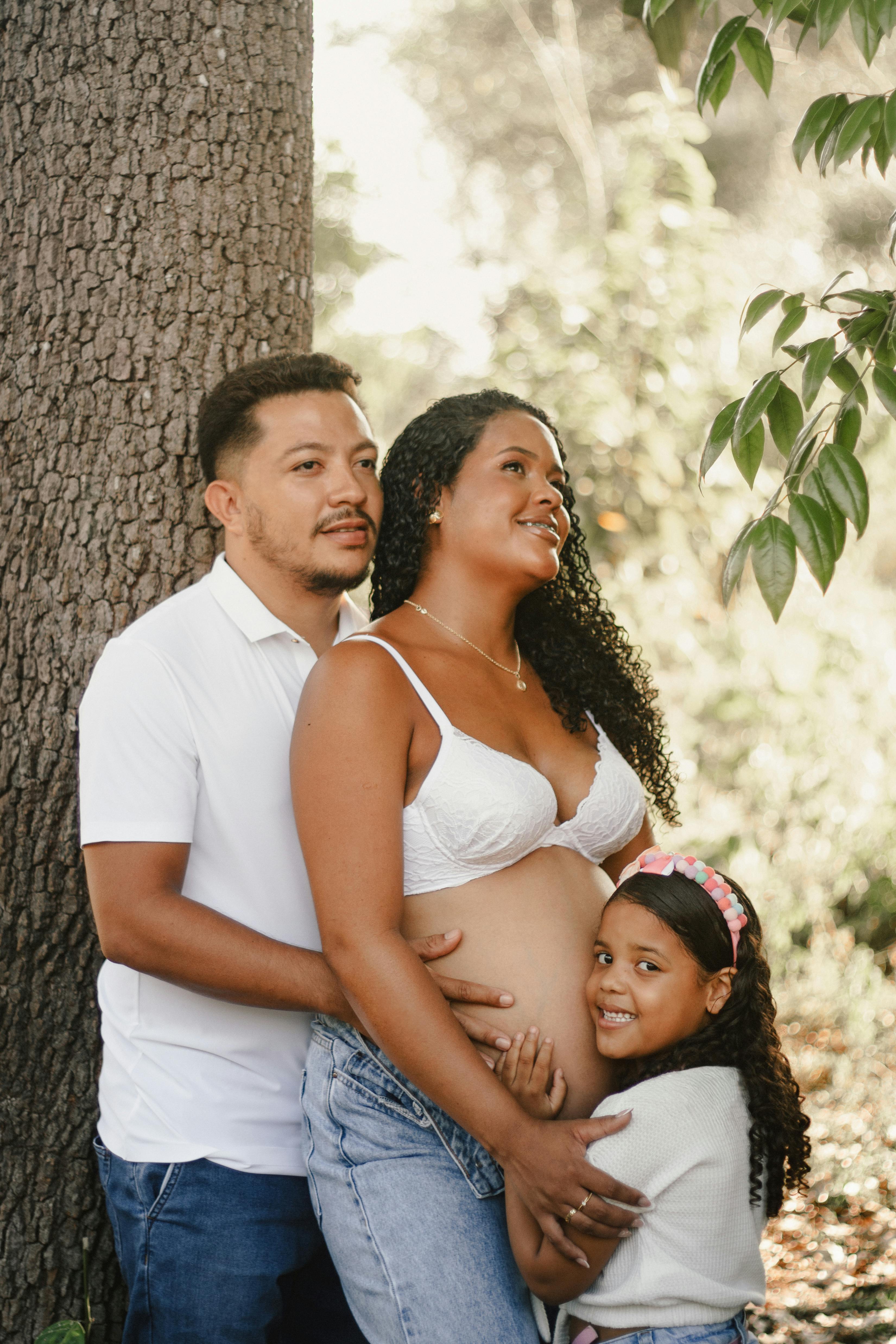 Free A family celebrates an upcoming addition with an outdoor maternity portrait under a tree. Stock Photo