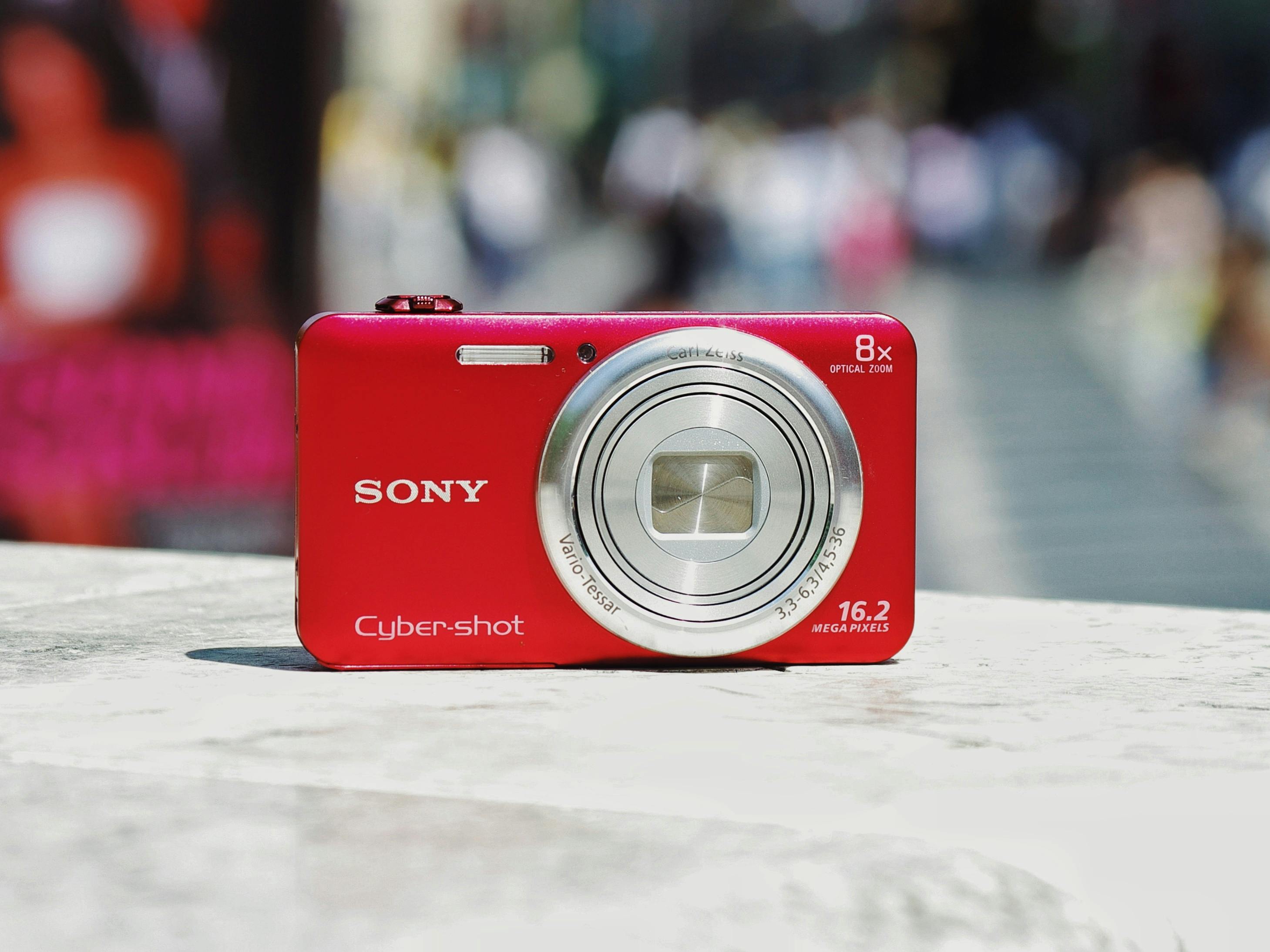 A vibrant red compact digital camera with blurred urban background, ideal for lifestyle or tech imagery.