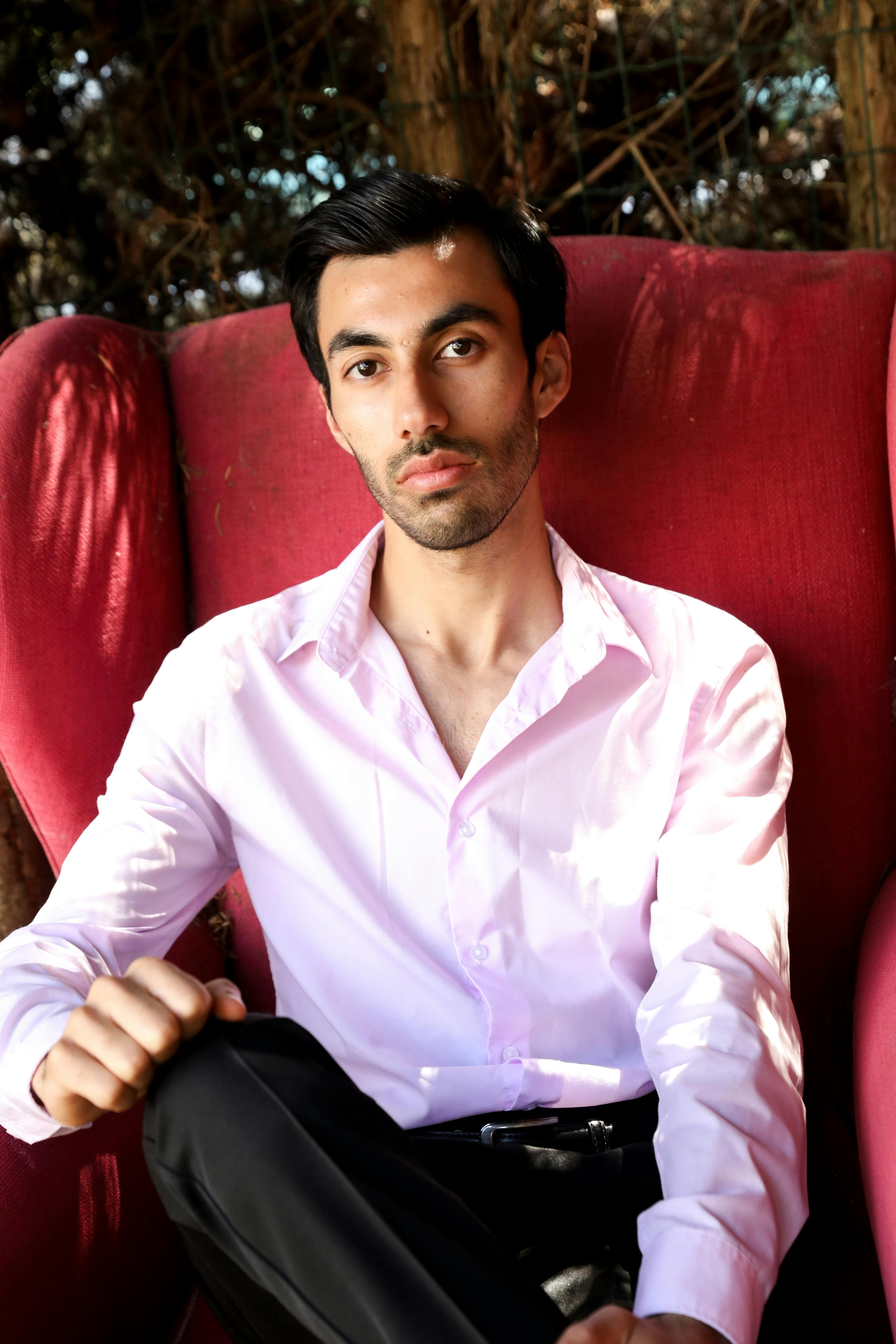 Stylish young man in a white shirt seated in a red armchair, outdoors.