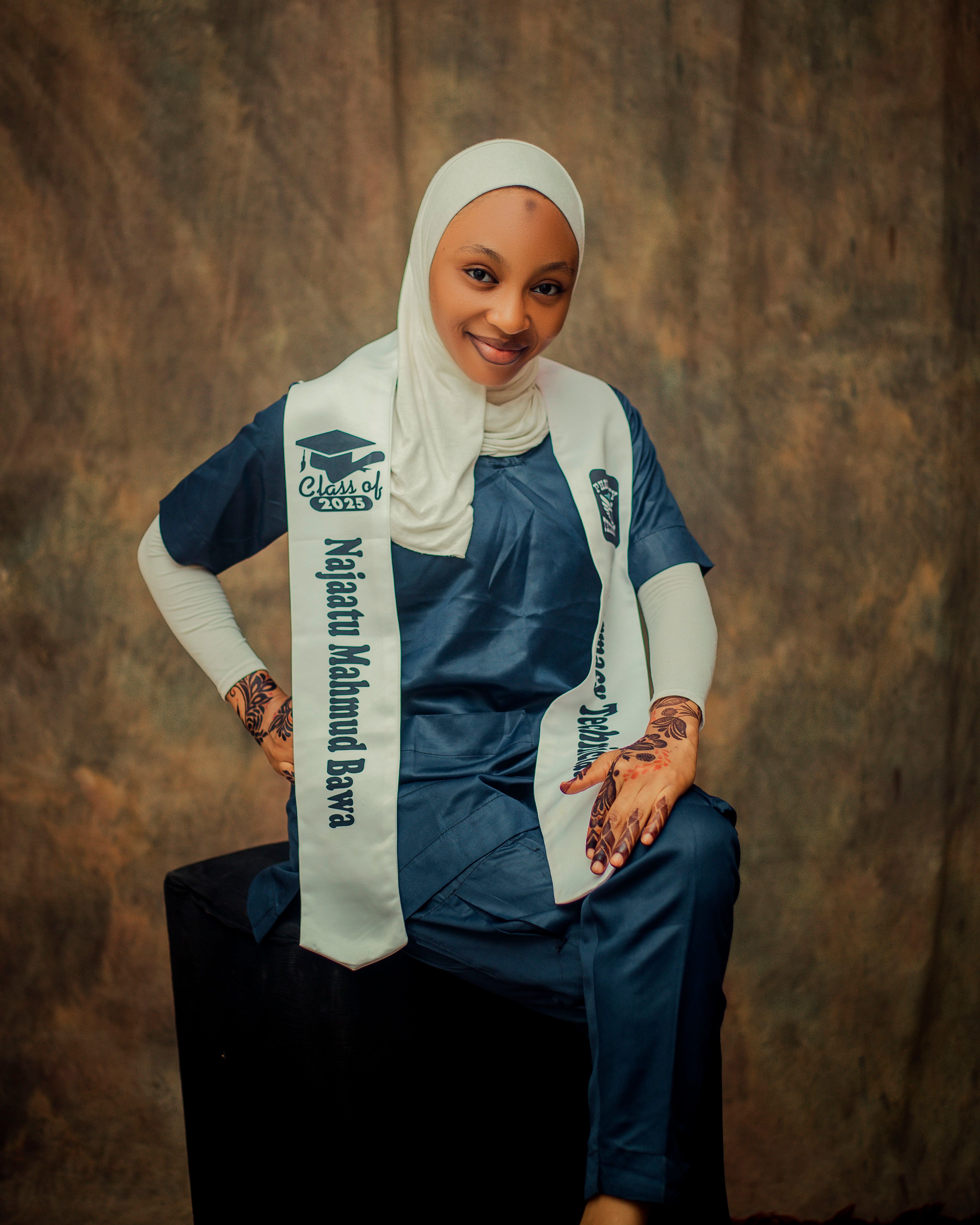 A young Nigerian woman in traditional attire and henna proudly displays her graduation stole indoors.