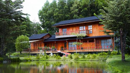 Free A picturesque wooden house surrounded by lush greenery reflected in a serene lake, evoking tranquility and natural beauty. Stock Photo