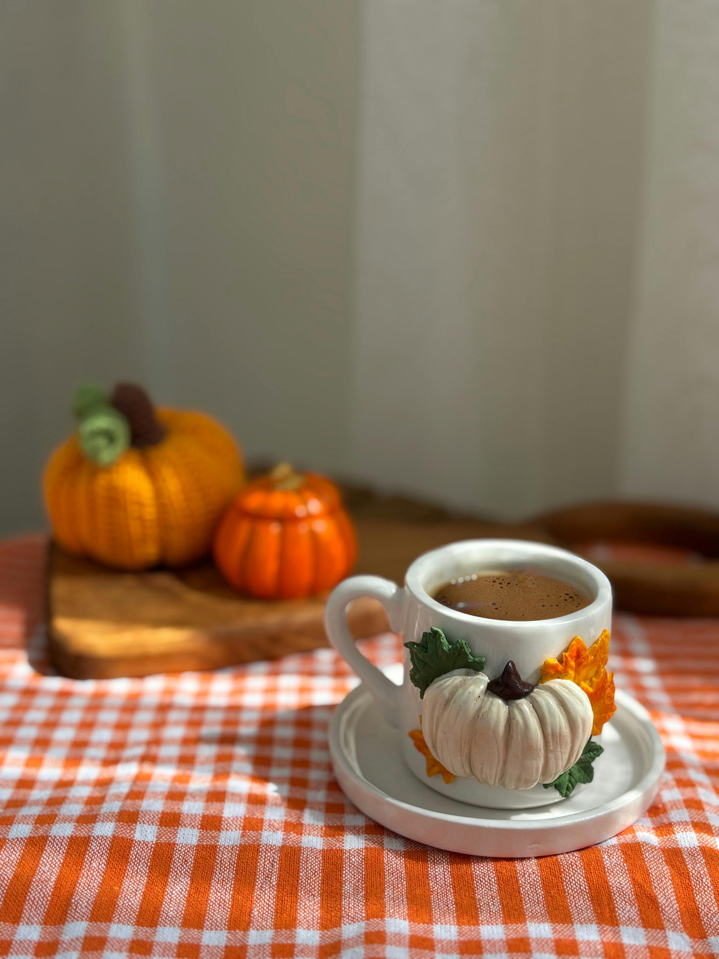 Cozy coffee cup with autumn decoration and pumpkins on a gingham tablecloth.